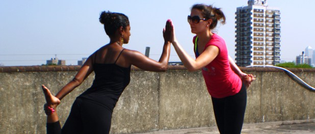 Two women practice Dru Yoga, partner assisted Dancer posture on the roof of a car park in Peckham.